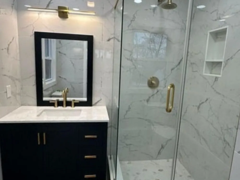 Bathroom renovation featuring a modern vanity and glass shower with gold details.