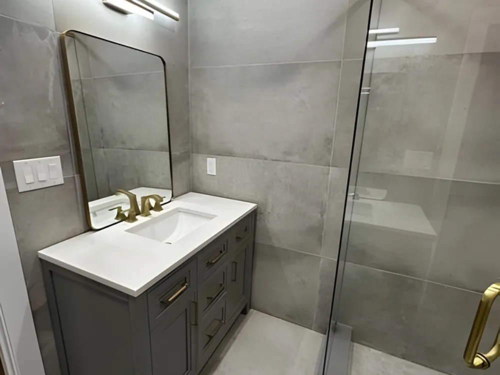 Modern bathroom renovation featuring vanity with brass accents and frameless glass shower.